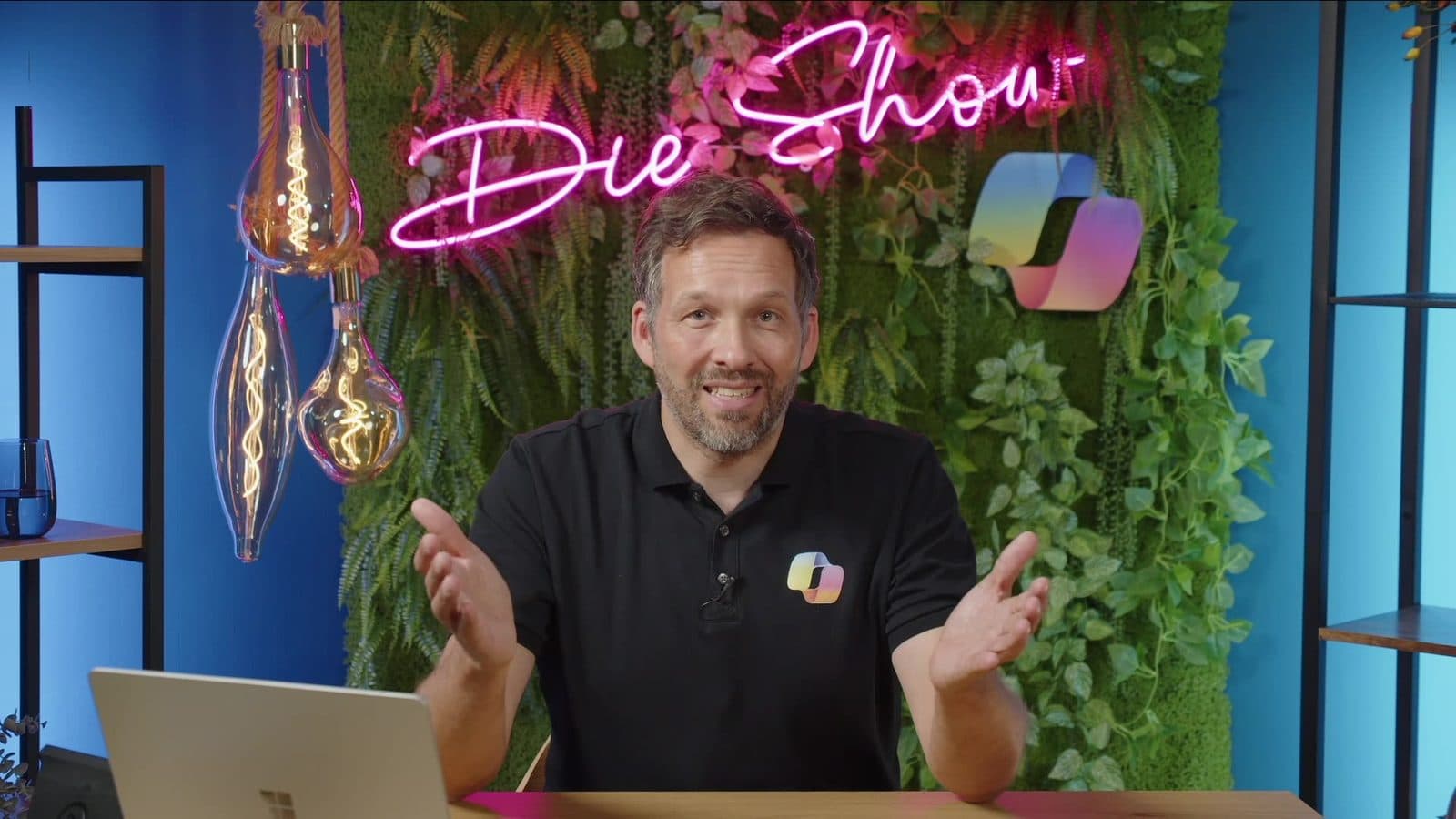 Alexander Eggers moderiert Die Copilot Show im Studio, hinter ihm der Neon-Schriftzug „Die Show“